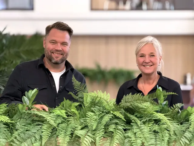To personar smiler til kamera ved grøne planter.